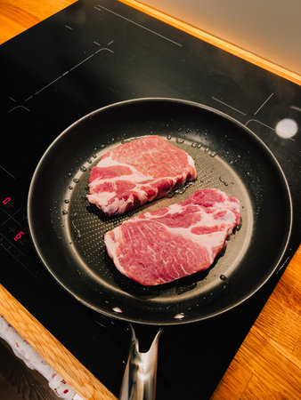 Two pork chops sizzling in pan on modern induction stove, creating enticing scene of meal preparation in bright, contemporary kitchen. Aroma of cooking meat fills air. Sizzling pork chops browningの写真素材