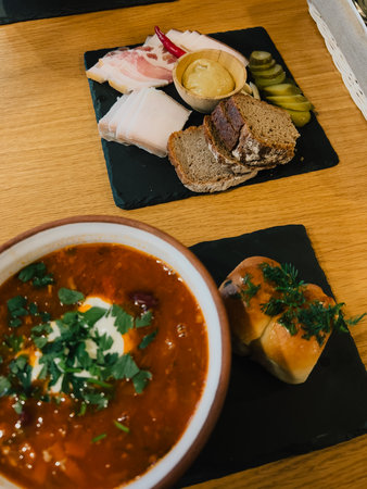Ukrainian soup with sour cream and herbs, accompanied by bread and platter of salo, rye bread, pickled cucumbers, mustard, and chili pepper, served on black slate plates. Traditional Ukrainian mealの写真素材
