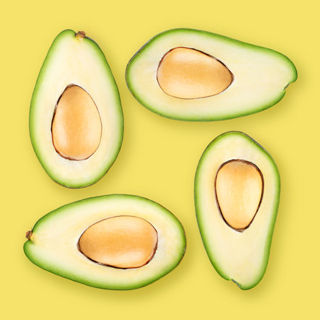 Four ripe avocado halves on yellow background.