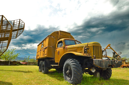 Old yellow truck on a green meadow with cloudy sky background.の写真素材