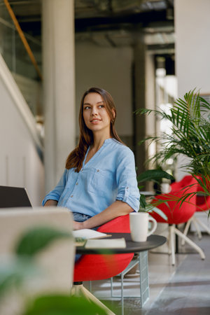 A businesswoman works in a modern office with a laptop and coffee for productivity