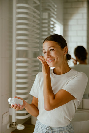 A woman is applying her skincare routine in a beautifully designed modern bathroom spaceの写真素材