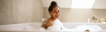 A woman smiles while bathing in a foamy tub for comfort and happinessの写真素材