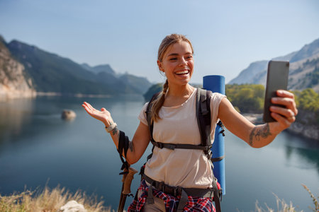 A joyful hiker takes a selfie by a stunning lake surrounded by majestic mountainsの写真素材