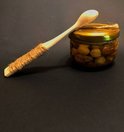 wooden spoon with a jar of honey with nuts on a black backgroundの写真素材
