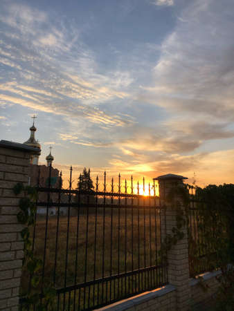 sunset among the clouds behind a metal fence with ivyの写真素材