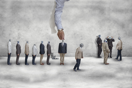 A giant hand is screwing nuts onto the human necks in the form of boltsの写真素材