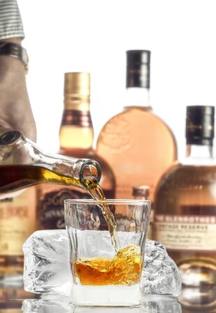 Hand pouring alcohol into a glass on the background of bottlesの写真素材