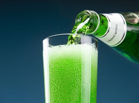 Tarragon carbonated drink is pouring from a bottle into a glass