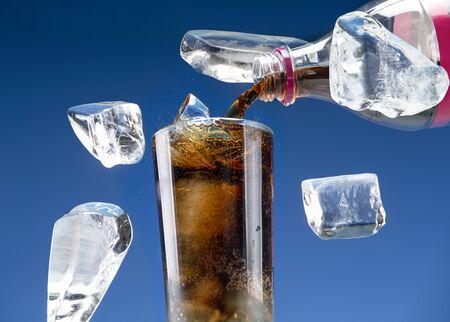 Carbonated drink is poured from a plastic bottle into a glass with iceの写真素材