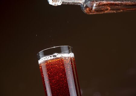 Carbonated cherry drink pouring from a bottle into a glassの写真素材