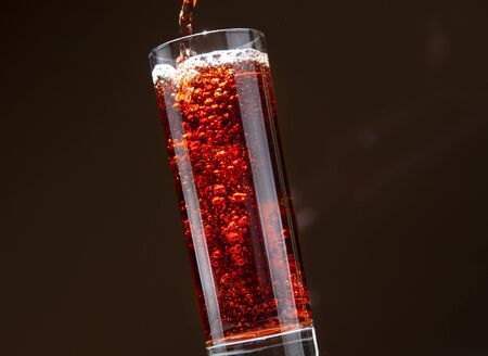 Carbonated cherry drink pouring from a bottle into a glass