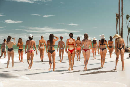 Girls and women in swimsuits perform group exercises on a tropical beach