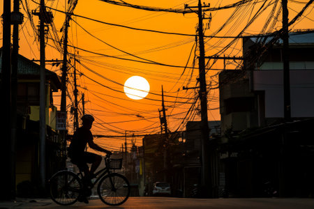 silhouette of a cyclist riding a bicycle on an asphalt road in orange twilight against the sunset skyの素材