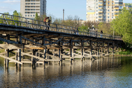 A charming wooden pedestrian bridge stretches across the river, its weathered planks providing a rustic path through nature. The serene flow of the river beneath adds to the tranquil atmosphereの写真素材