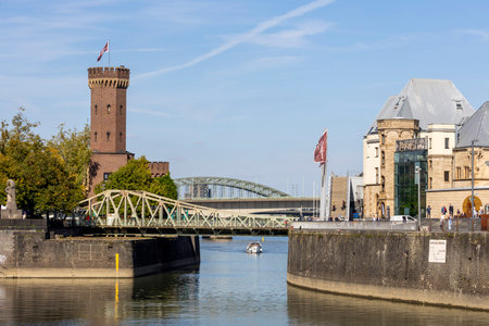 A scenic view of Cologne and the Rhine River unfolds near the Chocolate Museum, where boats glide gently across the shimmering water. The modern buildings and bridges blend with historic charm under a bright, clear sky.の写真素材