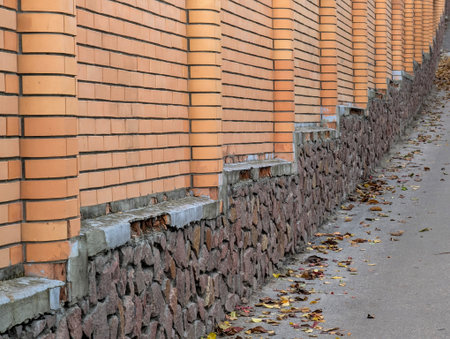 A red brick fence with a stone foundation lines a street that slopes upward, creating a textured urban scene with classic architectural detail.の写真素材