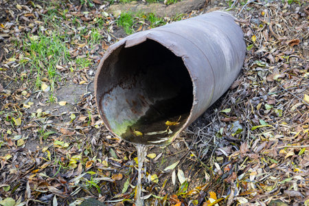 An old iron drain pipe leaks water, with drops glistening in the light, showing age, decay, and the...