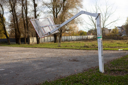 A broken and lopsided basketball hoop stands on an open-air sports court, symbolizing energy,...