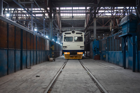 The electric train is parked on the grounds of a construction and repair plant, surrounded by...