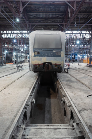 The electric train is parked on the grounds of a construction and repair plant, surrounded by machines, tools and industrial equipment in the workshop.の写真素材