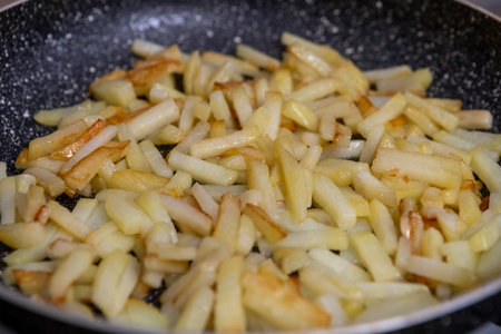 Potato slices are fried in a pan until golden and crispy, with appetizing texture and warm kitchen...