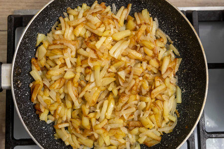 Potato slices with onions are fried in a pan until golden and crispy, with appetizing texture and...
