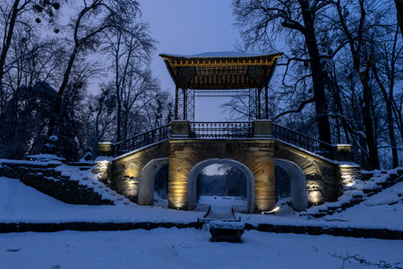 Evening view of an oriental bridge in a winter park, featuring classic Chinese design and decorative lighting. The soft glow highlights the curved roof and intricate details, offering a tranquil and picturesque scene.のeditorial素材