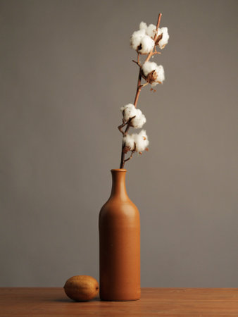 Cotton branch in brown vase on wooden table on gray backgroundの写真素材
