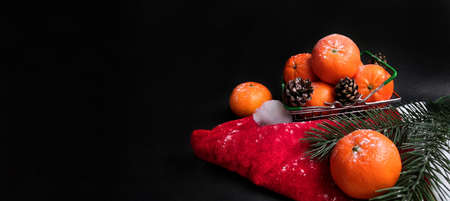 Christmas tangerines in a small grocery cart on a Santa hat on an black background, Christmas fruits, Merry Christmas, New year and tangerines, place for textの写真素材