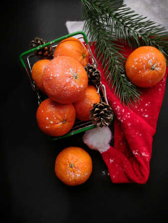 Christmas tangerines in a small grocery cart on a Santa hat on an black background, Christmas fruits, Merry Christmas, New year and tangerines, place for textの写真素材