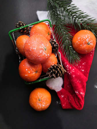 Christmas tangerines in a small grocery cart on a Santa hat on an black background, Christmas fruits, Merry Christmas, New year and tangerines, place for textの写真素材