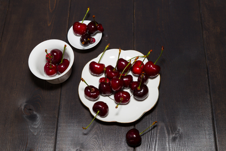 Berries of sweet cherry on a wooden table in a white bowl. Bright burgundy juicy berries. Dark background.の写真素材