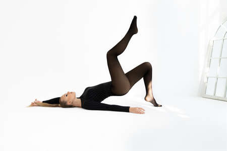 fashion model in black tights on the white background. Acrobatic dancing woman posing. hot blonde girl with long legs in lingerieの写真素材
