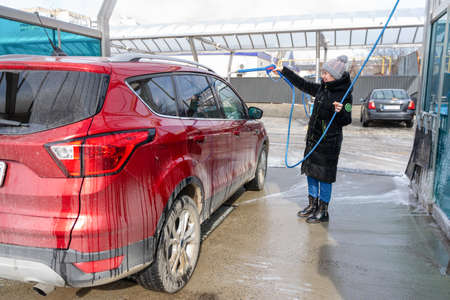 washing car at autowash. Car wash. red machine under the pressure of water at a car wash. car in foam. woman washing carの写真素材