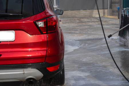 washing car at autowash. Car wash. red machine under the pressure of water at a car wash. car in foam. woman washing carの写真素材