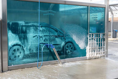 washing car at autowash. Car wash. red machine under the pressure of water at a car wash. car in foam. woman washing carの写真素材
