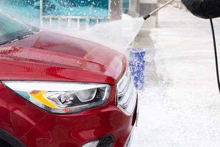 washing car at autowash. Car wash. red machine under the pressure of water at a car wash. car in foam. woman washing carの写真素材