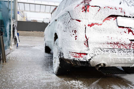 washing car at autowash. Car wash. red machine under the pressure of water at a car wash. Red car in foamの写真素材
