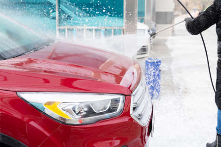 washing car at autowash. Car wash. red machine under the pressure of water at a car wash. car in foam. woman washing carの写真素材