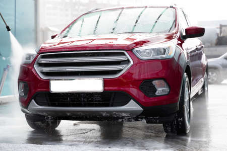 washing car at autowash. Car wash. red machine under the pressure of water at a car wash. car in foam. woman washing carの写真素材