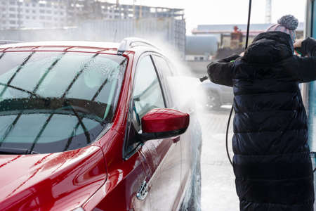 washing car at autowash. Car wash. red machine under the pressure of water at a car wash. car in foam. woman washing carの写真素材