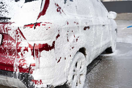 washing car at autowash. Car wash. red machine under the pressure of water at a car wash. car in foam. woman washing carの写真素材