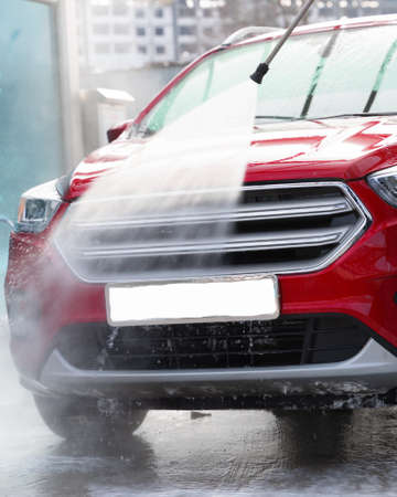 washing car at autowash. Car wash. red machine under the pressure of water at a car wash. car in foam. woman washing carの写真素材