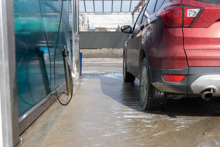 washing car at autowash. Car wash. red machine under the pressure of water at a car wash. car in foam. woman washing carの写真素材