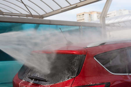 washing car at autowash. Car wash. red machine under the pressure of water at a car wash. car in foam. woman washing carの写真素材