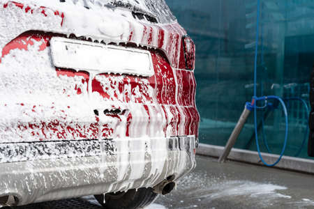 washing car at autowash. Car wash. red machine under the pressure of water at a car wash. car in foam. woman washing carの写真素材