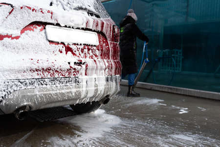 washing car at autowash. Car wash. red machine under the pressure of water at a car wash. car in foam. woman washing carの写真素材