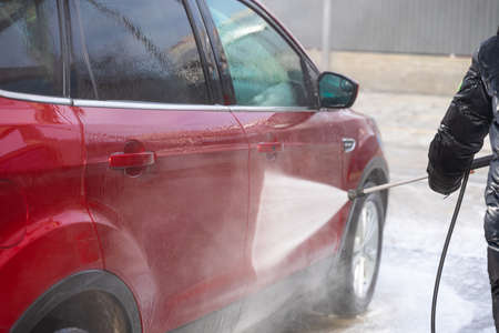 washing car at autowash. Car wash. red machine under the pressure of water at a car wash. car in foam. woman washing carの写真素材