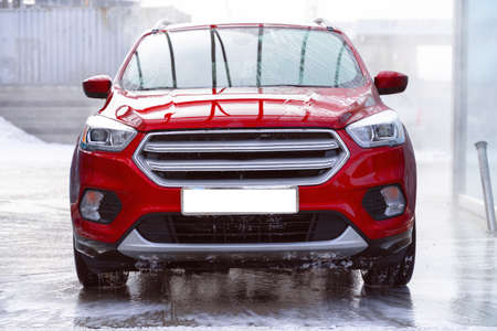 washing car at autowash. Car wash. red machine under the pressure of water at a car wash. car in...